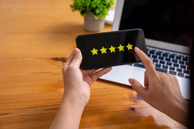 Person viewing a five-star customer rating on a smartphone beside a laptop