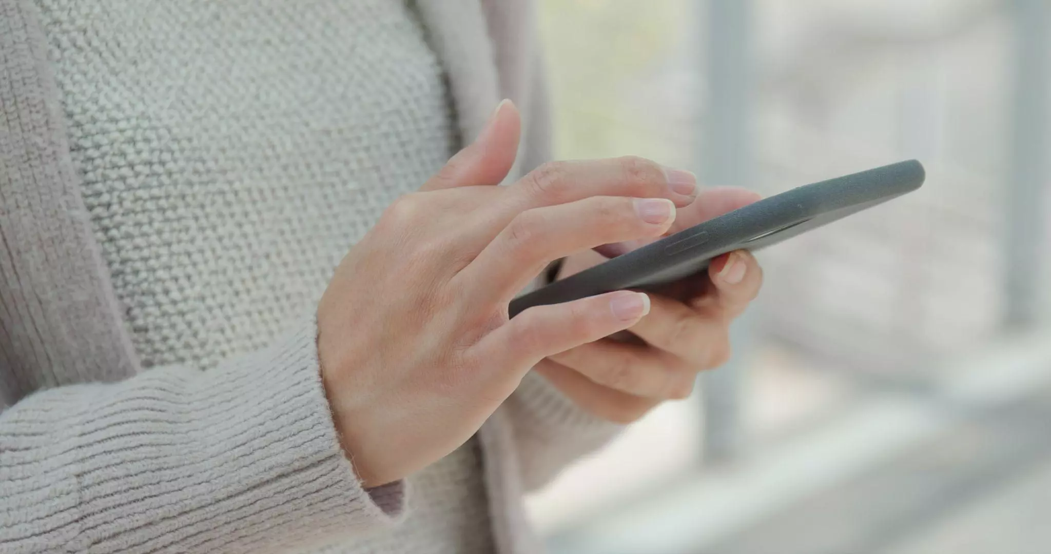 Woman Browsing on Smartphone Woman in a knit sweater using a smartphone, browsing on the screen